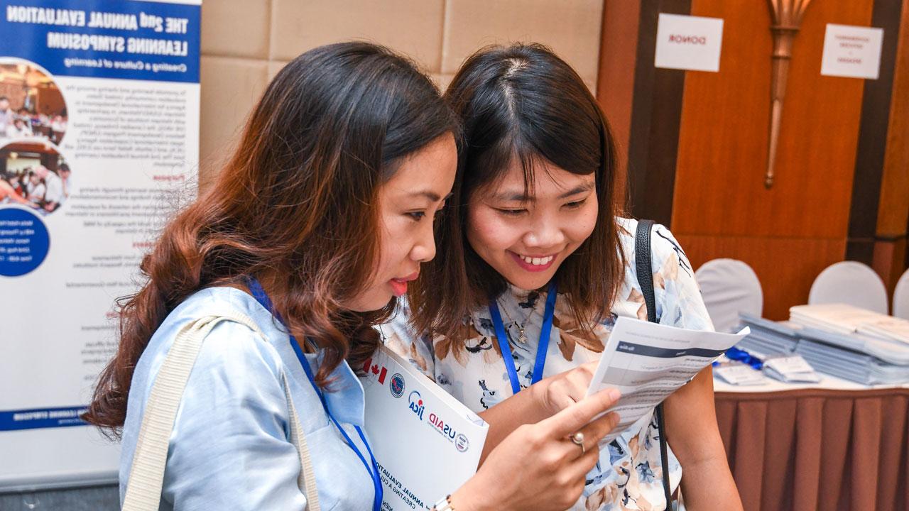 Two women stand close together looking at a piece of paper in Vietnam